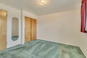 Primary bedroom with baseboards, a textured ceiling, carpet, and a closet
