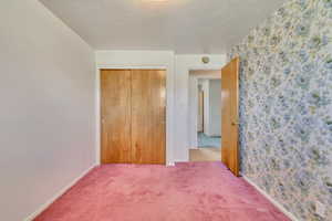 Unfurnished bedroom featuring a textured ceiling, carpet, baseboards, wallpapered walls, and a closet