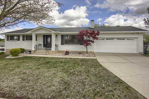 Single story home with a garage, a front lawn, a chimney, brick siding, and driveway