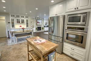 Kitchen with stainless steel appliances, white cabinetry, stone finish flooring, recessed lighting, and glass insert cabinets