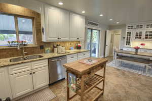 Kitchen featuring white cabinetry, decorative backsplash, a sink, and dishwasher