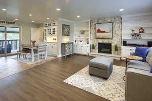 Living room with dark wood finished floors, a stone fireplace, built in features, recessed lighting, and ornamental molding