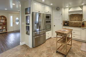Kitchen featuring white cabinets, appliances with stainless steel finishes, custom exhaust hood, and ornamental molding