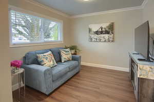Living area with baseboards, ornamental molding, and wood finished floors