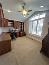 Office area featuring ceiling fan, light colored carpet, built in study area, baseboards, and vaulted ceiling