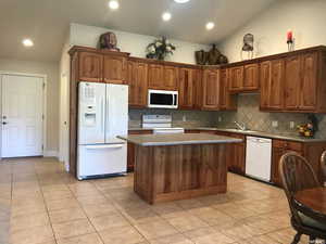 Kitchen with island, vaulted ceiling, a kitchen island, white appliances, and tasteful backsplash
