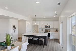 Kitchen featuring a kitchen breakfast bar, light wood-type flooring, white cabinetry, a sink, and stainless steel appliances