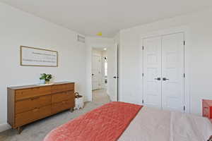 Bedroom with light colored carpet, baseboards, visible vents, and a closet