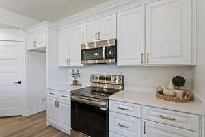 Kitchen with light countertops, appliances with stainless steel finishes, white cabinets, and light wood-type flooring