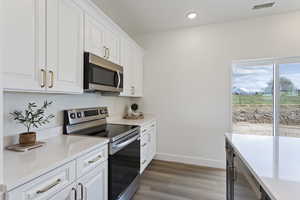 Kitchen with appliances with stainless steel finishes, light countertops, white cabinetry, baseboards, and light wood-type flooring