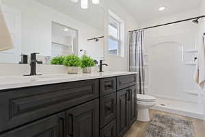 Bathroom with a sink, double vanity, toilet, wood finished floors, and a stall shower