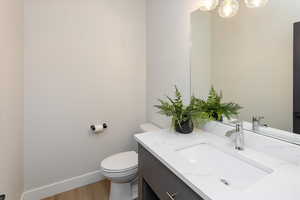 Half bathroom featuring wood finished floors, vanity, baseboards, toilet, and a notable chandelier