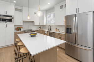 Kitchen featuring a sink, light wood-style floors, stainless steel appliances, decorative backsplash, and a kitchen bar