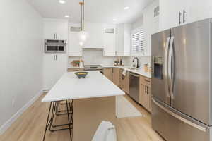 Kitchen featuring a kitchen breakfast bar, appliances with stainless steel finishes, a sink, glass insert cabinets, and light wood-style flooring