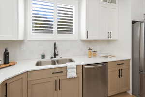 Kitchen with white cabinets, appliances with stainless steel finishes, a sink, light countertops, and decorative backsplash