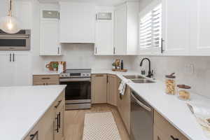 Kitchen with a sink, light countertops, stainless steel appliances, and glass insert cabinets