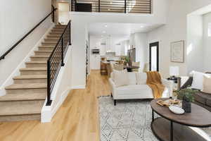Living room featuring stairs, baseboards, a high ceiling, light wood-type flooring, and recessed lighting