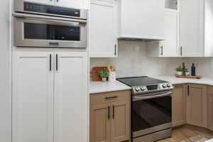 Kitchen featuring light countertops, backsplash, appliances with stainless steel finishes, and white cabinetry