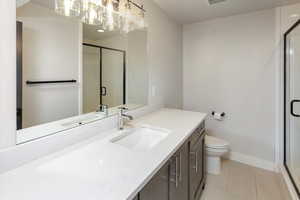 Bathroom with tile patterned flooring, a stall shower, vanity, toilet, and an inviting chandelier