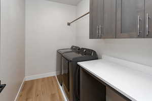 Laundry area with light wood-style floors, separate washer and dryer, baseboards, and cabinet space