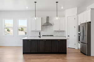 Kitchen featuring wall chimney range hood, stainless steel refrigerator with ice dispenser, white cabinetry, and light countertops