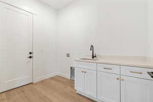 Washroom with light wood-style floors, baseboards, cabinet space, a sink, and washer hookup