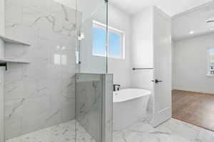 Bathroom with a healthy amount of sunlight, baseboards, tiled shower, and a freestanding bath