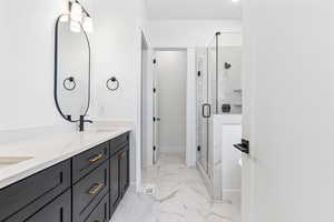 Full bathroom with a sink, double vanity, marble finish floor, baseboards, and a shower stall