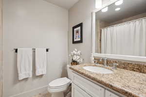 Bathroom featuring vanity, baseboards, curtained shower, and toilet