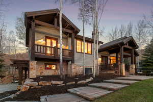 Back of house at dusk featuring covered porch, a balcony, and stone siding