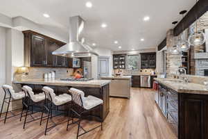 Kitchen featuring island exhaust hood, appliances with stainless steel finishes, a sink, a peninsula, and glass insert cabinets