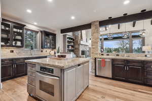 Kitchen with a sink, glass insert cabinets, stainless steel appliances, and light wood finished floors
