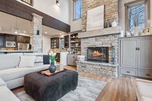 Living room featuring light wood-style flooring, a stone fireplace, and a towering ceiling