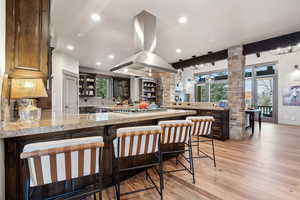 Kitchen with glass insert cabinets, island range hood, light wood finished floors, a peninsula, and stainless steel gas stovetop