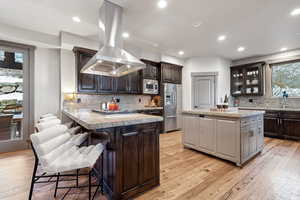 Kitchen with a kitchen breakfast bar, backsplash, island range hood, light countertops, and stainless steel appliances