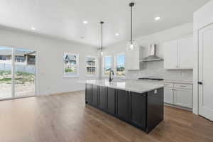 Kitchen with a sink, wall chimney exhaust hood, white cabinets, and light countertops