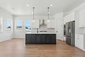 Kitchen with light countertops, wall chimney exhaust hood, appliances with stainless steel finishes, and white cabinetry
