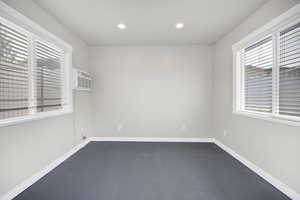 Unfurnished room featuring baseboards, a wall mounted AC, concrete flooring, and recessed lighting