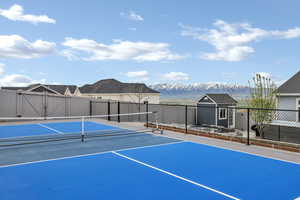 View of sport court with fence, a mountain view, an outbuilding, and a storage shed