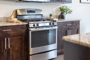 Kitchen with light stone counters, dark brown cabinetry, and stainless steel gas range oven