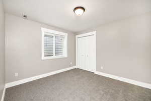 Unfurnished bedroom featuring baseboards, a closet, dark colored carpet, and visible vents