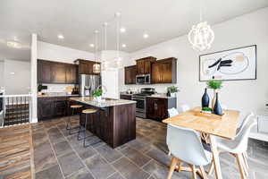 Kitchen with a kitchen island with sink, dark brown cabinetry, a breakfast bar, a chandelier, and appliances with stainless steel finishes