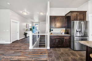 Kitchen with visible vents, dark brown cabinets, light stone countertops, stainless steel refrigerator with ice dispenser, and dark wood-type flooring