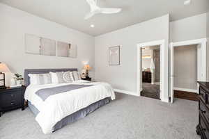 Bedroom with baseboards, light carpet, ceiling fan, and ensuite bathroom
