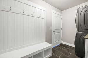 Clothes washing area with laundry area, a textured ceiling, stacked washing maching and dryer, baseboards, and dark tile patterned flooring