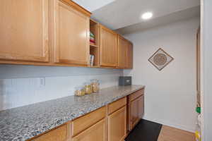 Kitchen featuring backsplash, open shelves, baseboards, light stone counters, and recessed lighting