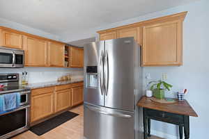 Kitchen with a textured ceiling, open shelves, light wood-type flooring, light stone counters, and stainless steel appliances
