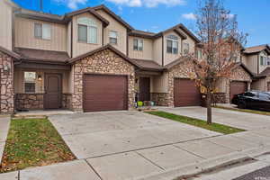 View of property with an attached garage, driveway, a shingled roof, and stone siding