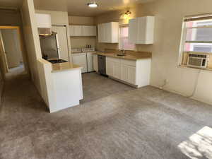 Kitchen featuring white cabinetry, washer and clothes dryer, carpet, stainless steel dishwasher, and a sink