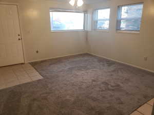 Spare room with light tile patterned flooring, ceiling fan, baseboards, and light carpet